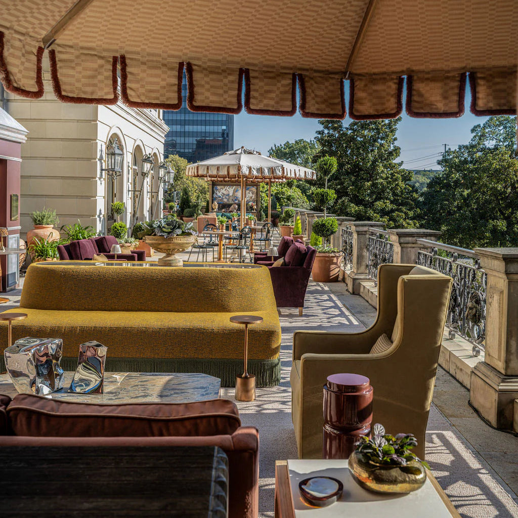 Outdoor patio with yellow sofa, armchair, and tables on a rooftop with cityscape view.