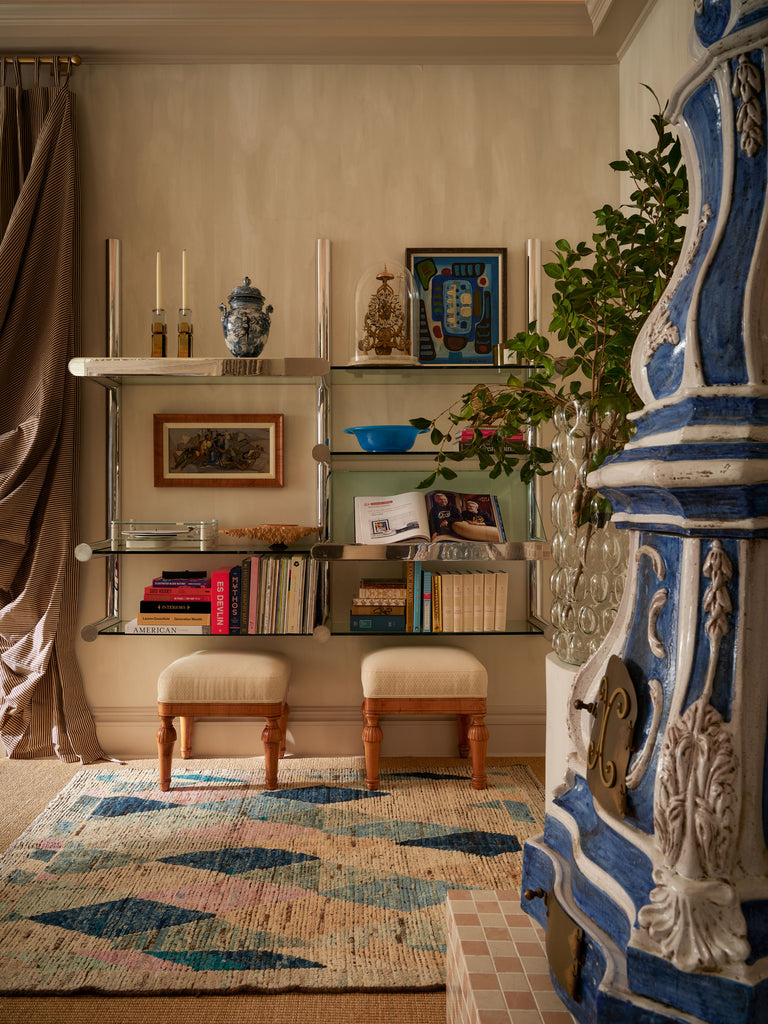 Decorative interior with a blue and white ornate stove, shelves with books and decor, and a patterned rug.