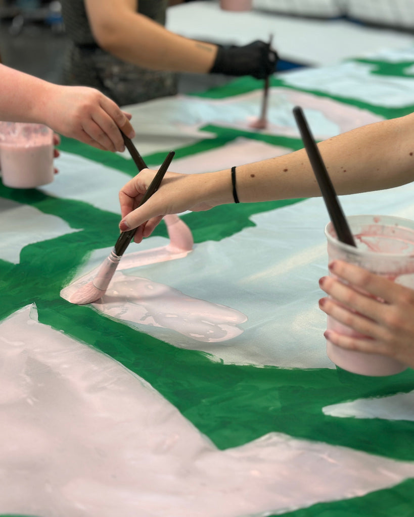 Three people painting on silk with brushes and cups of paint.