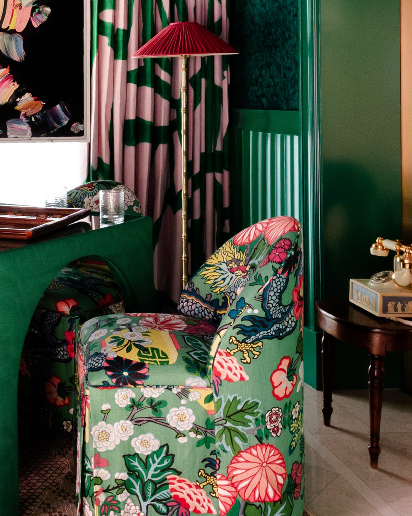 Decorative armchair with floral pattern in a room with green walls and a lamp.