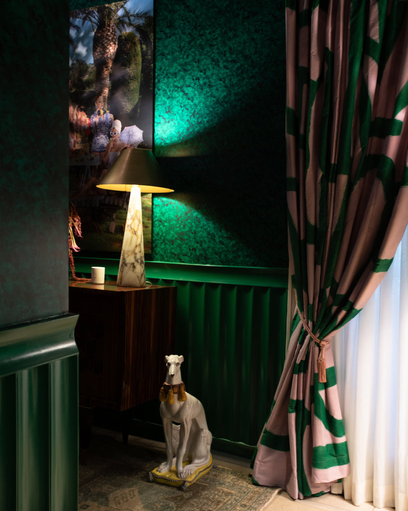 Decorative room with green walls, a lamp, a statue, and a patterned curtain.